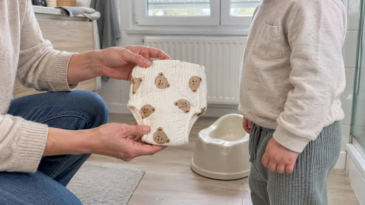 Un parent présente une culotte d'apprentissage en gaze de coton à un enfant habillé, dans la salle de bain