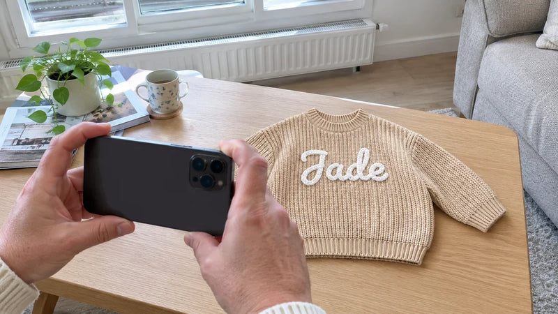 Photographier au téléphone un pull bébé brodé au prénom posé près d'une fenêtre