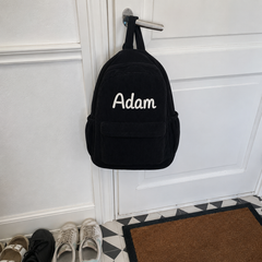 Photo client : sac à dos en velours côtelé noir avec le prénom Adam brodé main, accroché à la poignée de la porte d'entrée