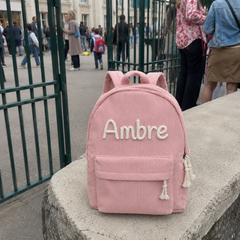 Photo client : sac à dos en velours côtelé rose avec le prénom Ambre brodé main, posé sur un muret devant l'école