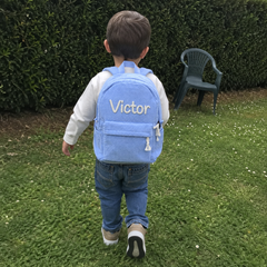 Photo client : garçon de dos dans le jardin avec son sac à dos en velours côtelé bleu ciel, prénom Victor brodé main