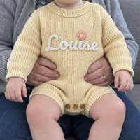 Un bebe sur les genoux de sa grand-mere, en barboteuse vanille, prenom Louise brode