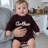 Un bebe porte dans les bras, en barboteuse chocolat au prenom Arthur brode