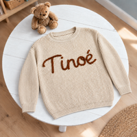 Pull bébé brodé main posé sur une table de chambre