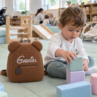 Enfant qui joue à la crèche à côté de son sac à dos ourson