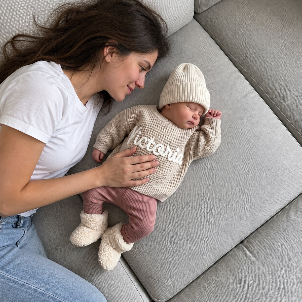 Une maman allongée près de son bébé endormi en pull beige avec le prénom Victoria brodé main