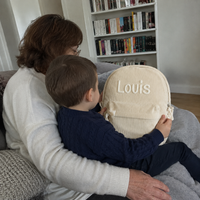 Grand-mère et son petit-fils sur le canapé découvrant ensemble le sac à dos en velours côtelé ivoire, prénom Louis brodé main en chaînette crème